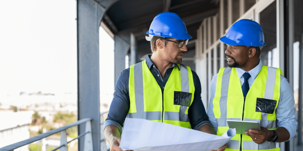 Architect reviewing construction blueprints at a project site with safety gear.