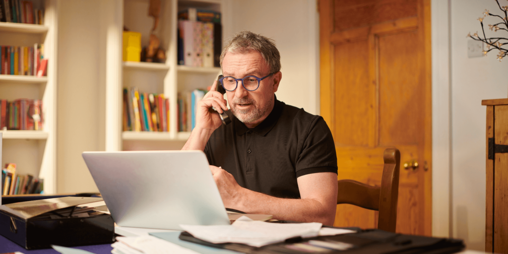 Self-employed professional using a laptop in a modern home office with a coffee cup and notepad.