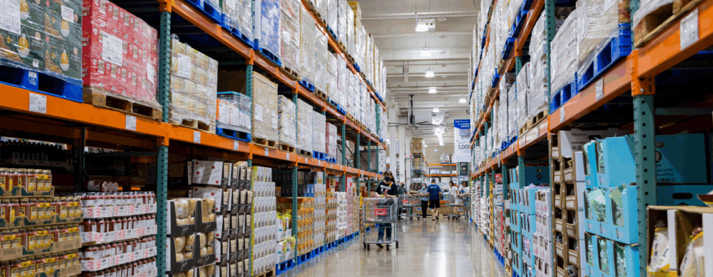 Busy wholesale warehouse aisle with stocked shelves and staff using trolleys, showing the need for Wholesale Insurance to protect goods and operations.