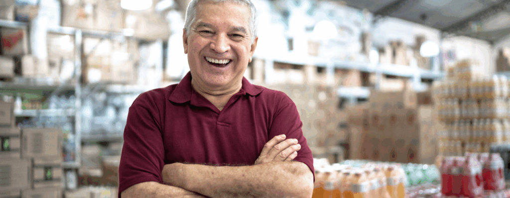 Smiling wholesale business owner standing with folded arms in a busy stockroom, representing the protection offered by Wholesale Insurance.
