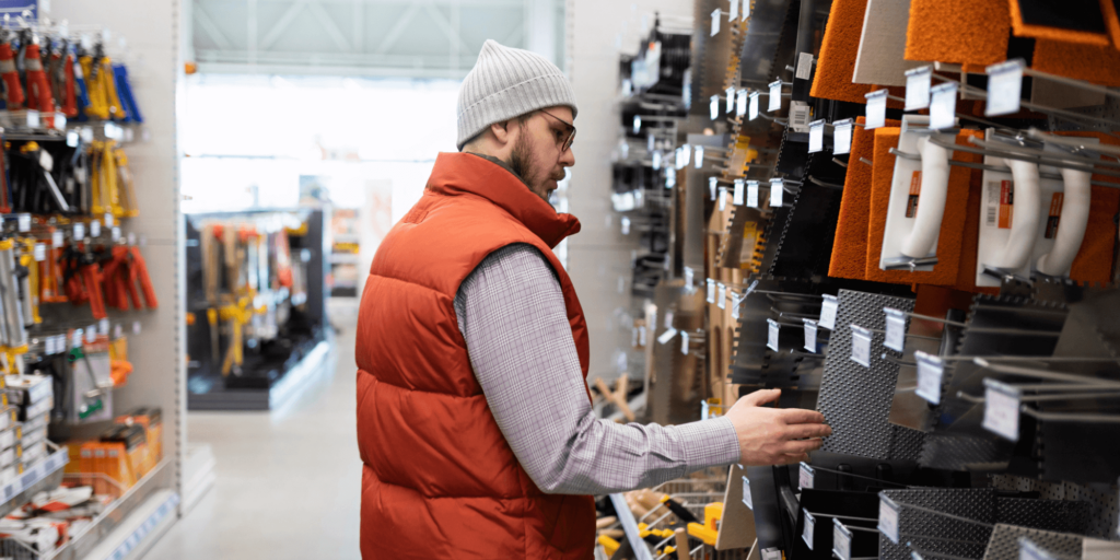 Man in an orange vest and gray beanie shopping for tools in a hardware store.